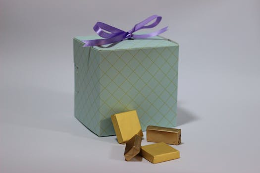 Cadeau en boîte bleue avec un ruban violet, accompagné de pralines dorées sur une surface neutre.